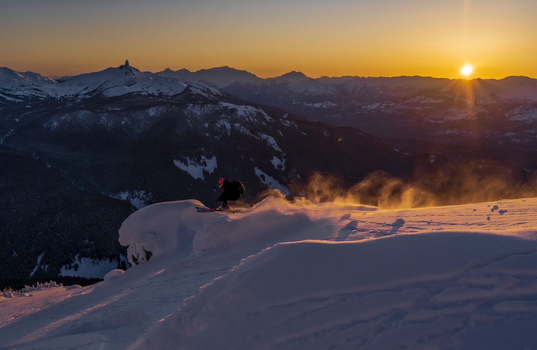 Skier dropping into a powder line at sunset with Black Tusk in the distance